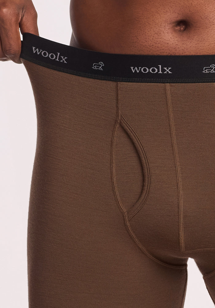 Close-up of a person wearing Woolx Backcountry Leggings in Bourbon Oak, stretching the black waistband to show fit—ideal as a merino wool base layer for cold weather or men’s backcountry leggings.