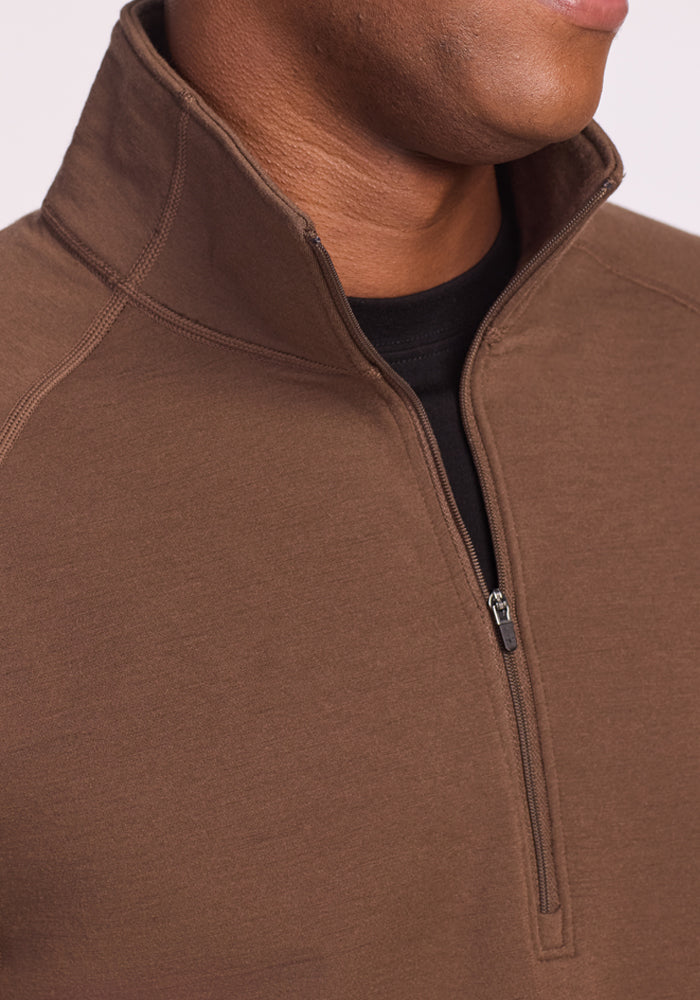 A person wears the Woolx Blizzard 1/4 Zip - Bourbon Oak over a black shirt. The image highlights the upper chest and neck, showcasing the partially open zipper and standing collar, with part of the person's face visible.