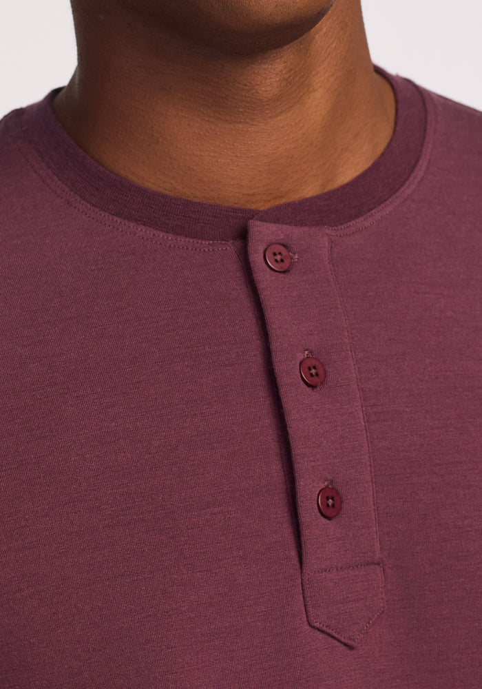 Close-up of a person wearing the Woolx Jackson Henley in Grape Harvest, featuring a round neckline and three buttons. The image highlights the shirt’s odor resistant and moisture wicking merino wool fabric.