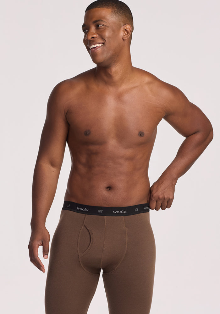 A fit, smiling man stands against a light background, wearing only Woolx Arctic Leggings in Bourbon Oak, featuring a black elastic waistband with the "woolx" logo.