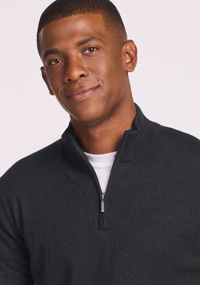 A man with short hair, slightly smiling, wears a Woolx Enzo Quarter Zip in Coal Stone over a white shirt, standing against a plain light background.