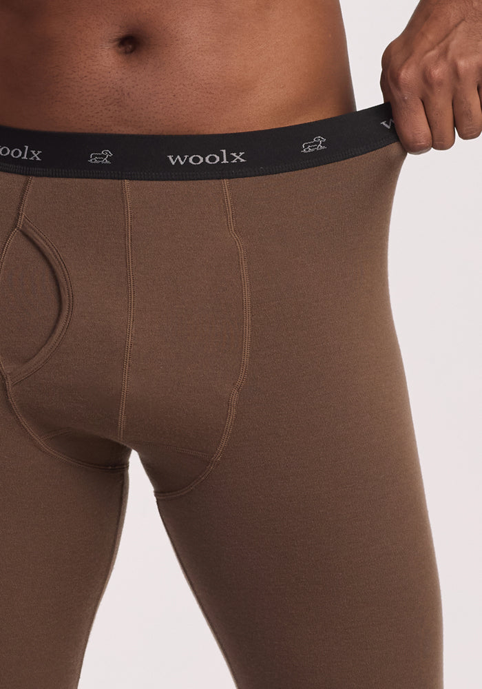 A person wearing Woolx Arctic Leggings in Bourbon Oak pulls out the waistband, revealing the “Woolx” name and logo on the black elastic band. The image highlights the waist and upper thigh of this Merino Wool Base Layer.