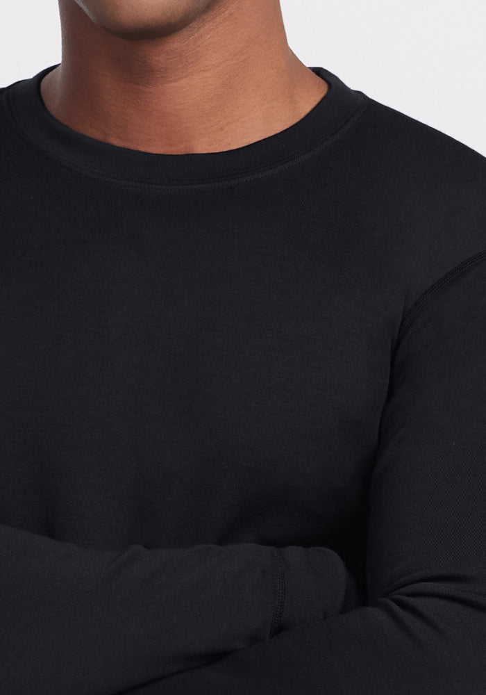 A person wearing the Woolx Glacier Long Sleeve Crew in black, arms crossed, is shown from shoulders to mid-torso against a light background.