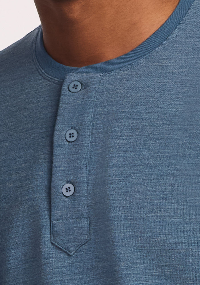 Close-up of a person wearing the Woolx Jackson Henley in Steel Blue, showcasing its three-button placket, textured merino wool fabric, and fine stitching. The moisture-wicking shirt is pictured without the person's face visible.