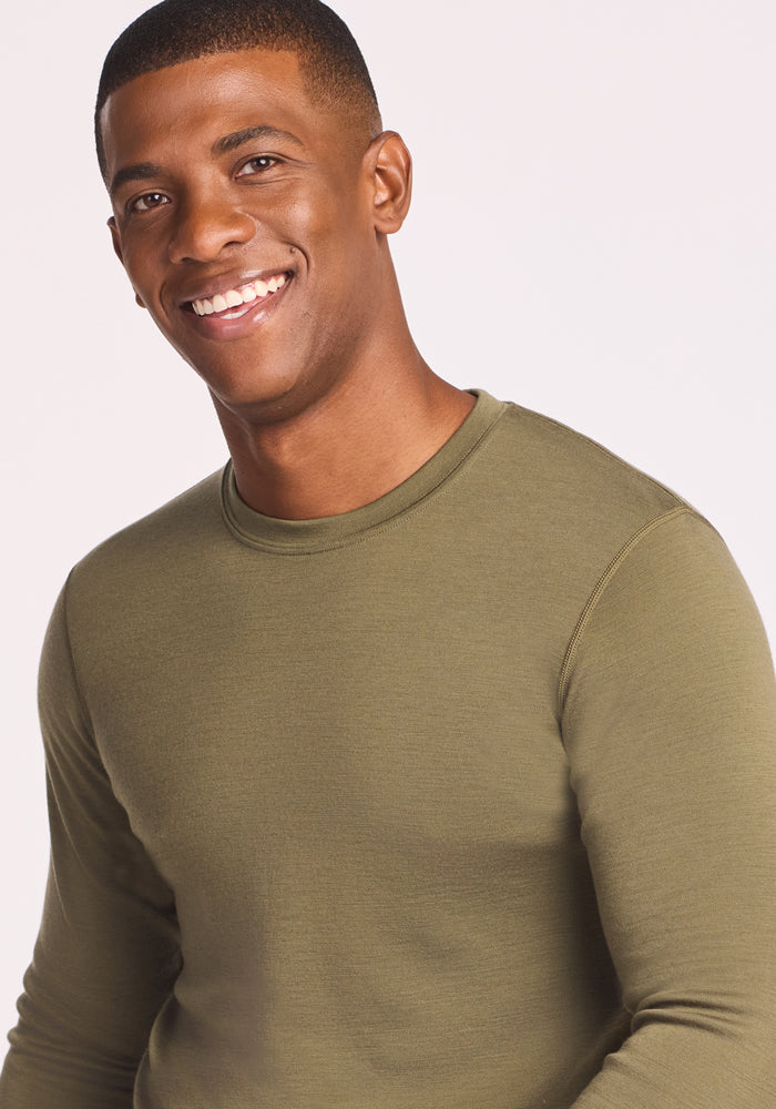 A man with short hair smiles at the camera wearing the Woolx Explorer Base Layer in Winter Moss against a light background.