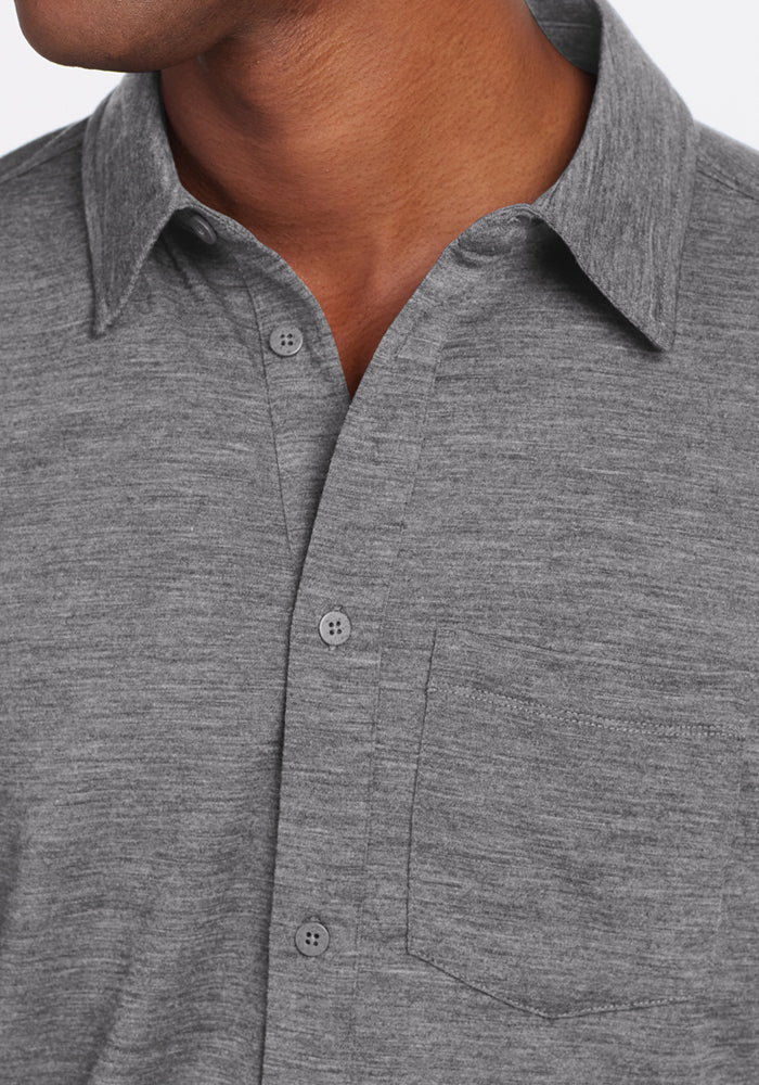 A close-up of a person wearing the Woolx Endi Full Button Down Shirt in Graphite Heather, showing the collared Merino wool shirt with a chest pocket. Only the lower face and neck are visible; the full face is not shown.