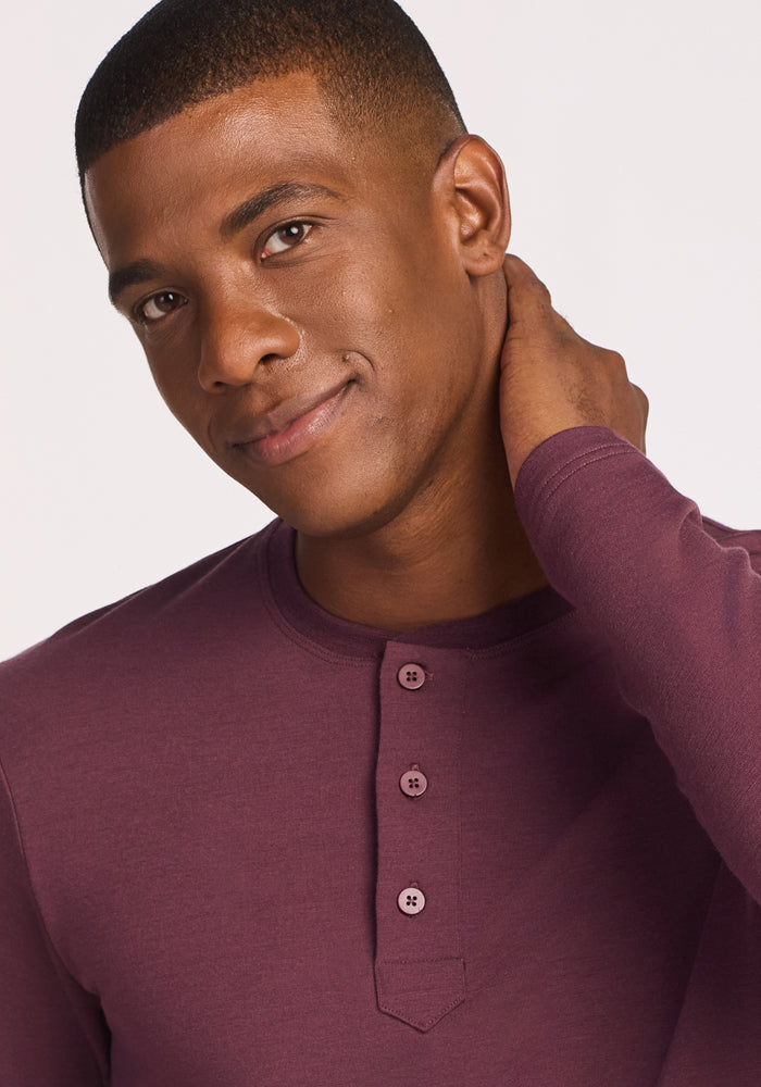 A man wearing the Woolx Jackson Henley in Grape Harvest smiles softly and touches the back of his neck against a plain white background.