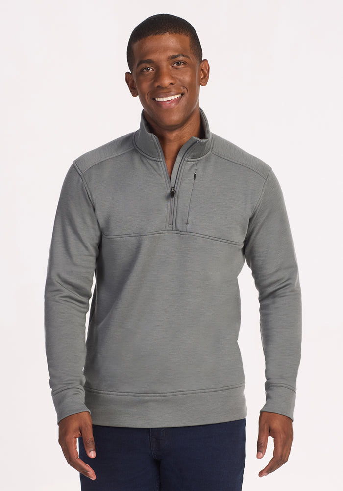 A man stands facing forward, smiling, wearing the Woolx Mason 1/4 Zip in Sedona Sage with dark jeans. His left hand is relaxed at his side against a plain white background. 