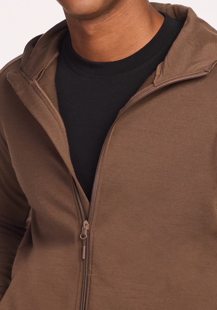 A person wears the Woolx Boulder Hoodie - Bourbon Oak, partially unzipped over a black t-shirt. The image focuses on the torso and part of the neck, highlighting the midweight brown men's zip-up hoodie.