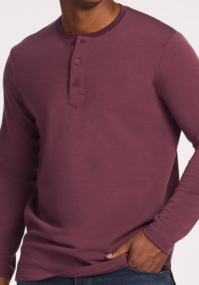 A man wears the Woolx Jackson Henley in Grape Harvest, a long-sleeve merino wool shirt with three buttons at the collar, paired with blue jeans.