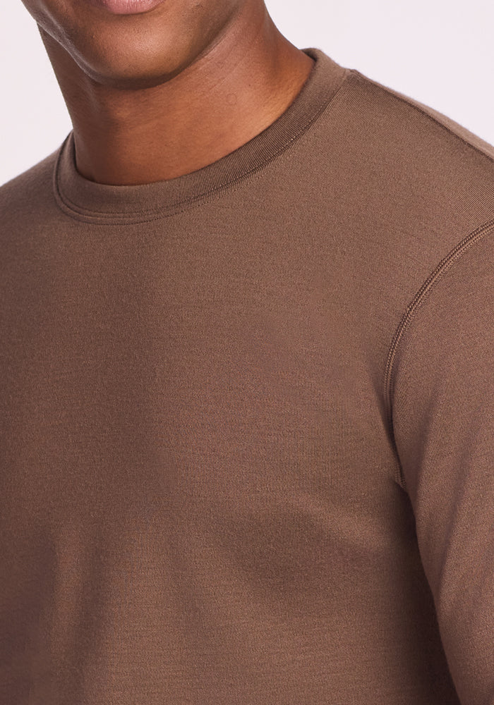 A close-up of a person wearing the Woolx Glacier Long Sleeve Crew in Bourbon Oak, shown from shoulders to mid-chest, with their face partially visible.