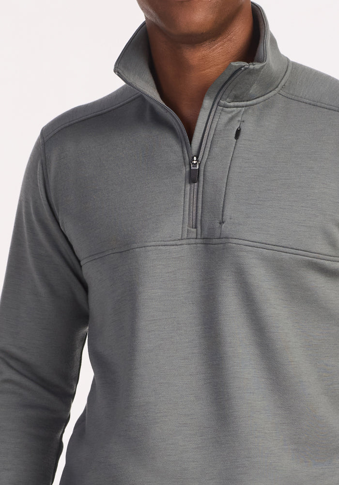 A person models the Woolx Mason 1/4 Zip in Sedona Sage—a light gray Merino wool pullover with a high collar and zippered chest pocket—ideal as a three-season layer, shown from shoulders to waist against a plain background.