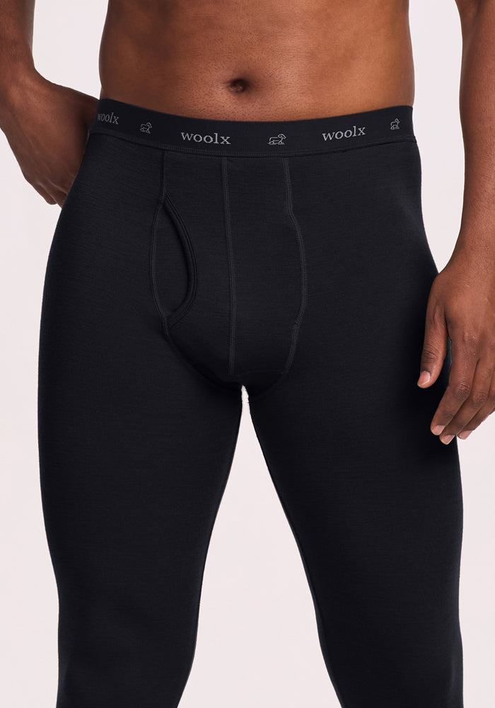 A person wears black Woolx Backcountry Leggings with a visible fly and branded elastic waistband. The cropped image (torso to thighs) showcases the fit, making these leggings perfect for cold weather activities.