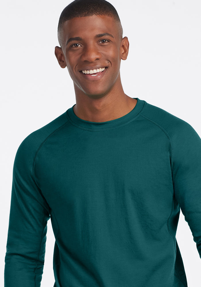 A man with short hair smiles at the camera, wearing the Woolx Essential Tee in Riverbank Green against a plain white background.