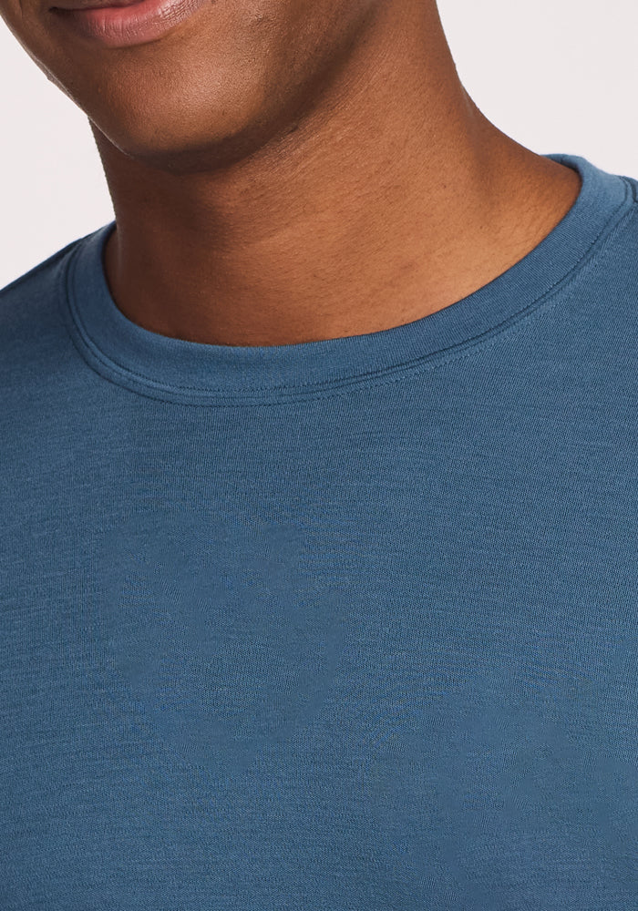 A close-up of a smiling person wearing the Woolx Easton Crew Neck Shirt in Steel Blue, showing only the lower half of their face, neck, and upper chest.