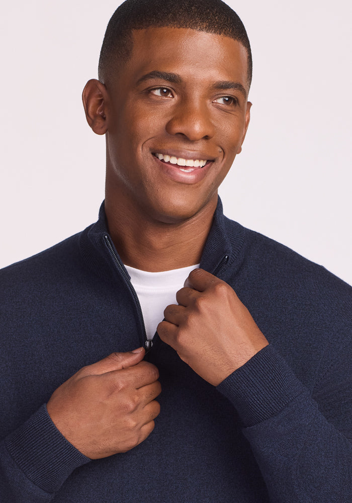 A smiling man wearing the Woolx Enzo Quarter Zip in Storm Cloud over a white shirt zips up the sweater while looking to the side, set against a light background.