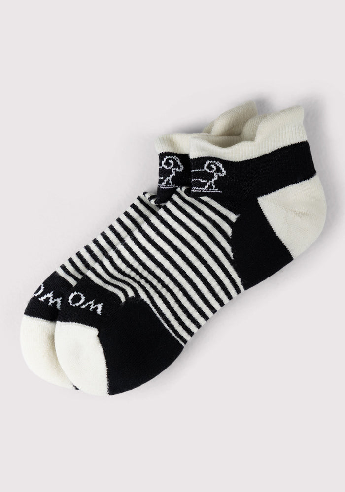 The Womens Amelia No Show Socks - Tuxedo Stripe by Woolx feature black and white stripes, a cushioned ankle design, solid black heel and toe, a small white detail near the cuff, and "Om" printed on the toes for style and comfort.