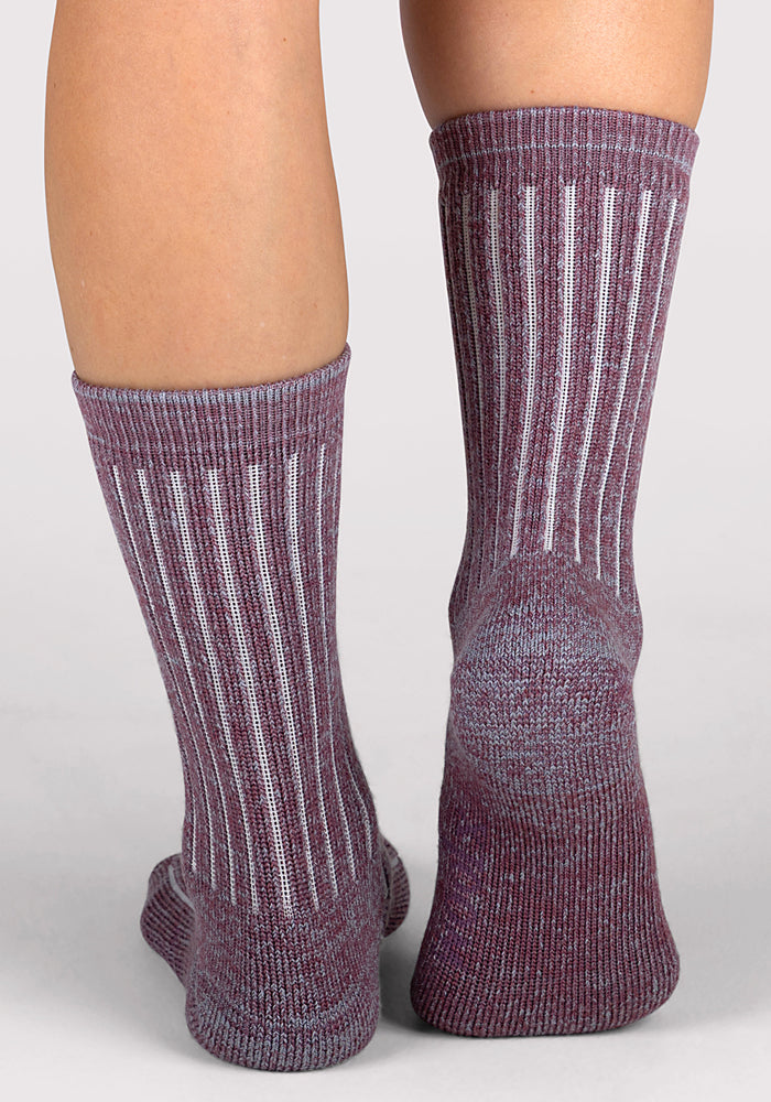 Close-up of the back of two legs wearing Woolx Womens Joey Crew Socks - Wildflower in ribbed maroon and gray with vertical white stripes and a textured knit pattern, standing on a light gray surface.