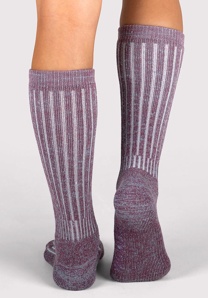 A close-up of two feet in Woolx Womens Joey Mid Calf Socks - Wildflower, featuring ribbed purple fabric with vertical white stripes, shown from the back against a plain light background.