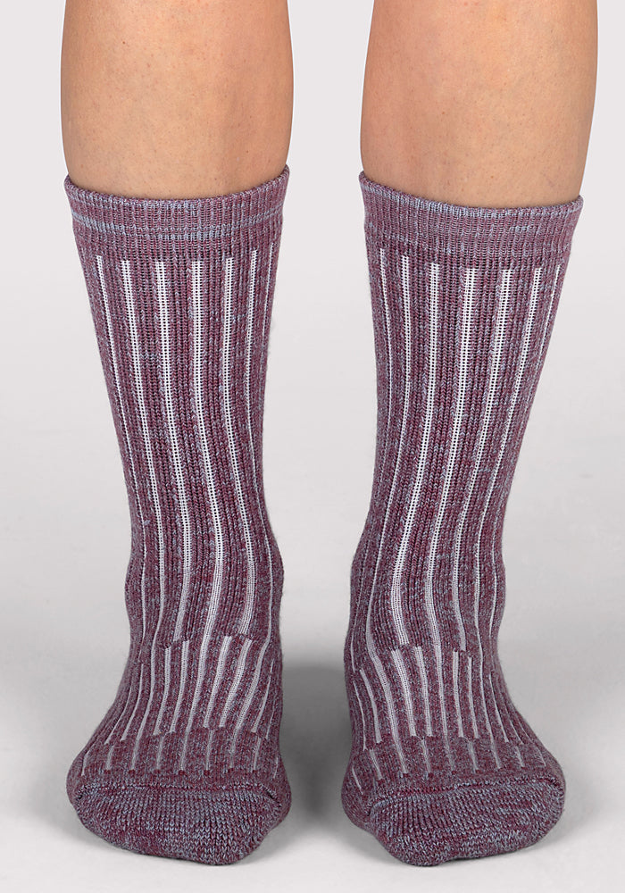 A pair of feet wearing Woolx Womens Joey Crew Socks - Wildflower in purple and white, featuring ribbed vertical stripes and a mid-calf fit, stands on a light gray surface.