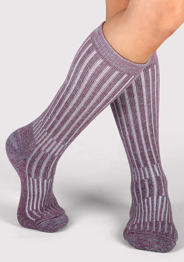 A person wears Woolx Womens Joey Mid Calf Socks - Wildflower, featuring a maroon and white striped pattern, with one leg crossed in front of the other against a light background.