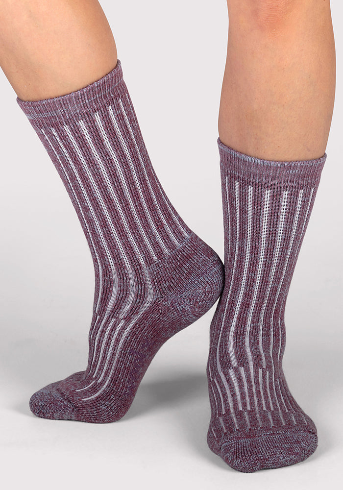 A person wearing Woolx Womens Joey Crew Socks in ribbed purple and white stripes stands on a light gray surface, with one foot flat and the other tiptoed, highlighting the cozy crew socks from multiple angles.