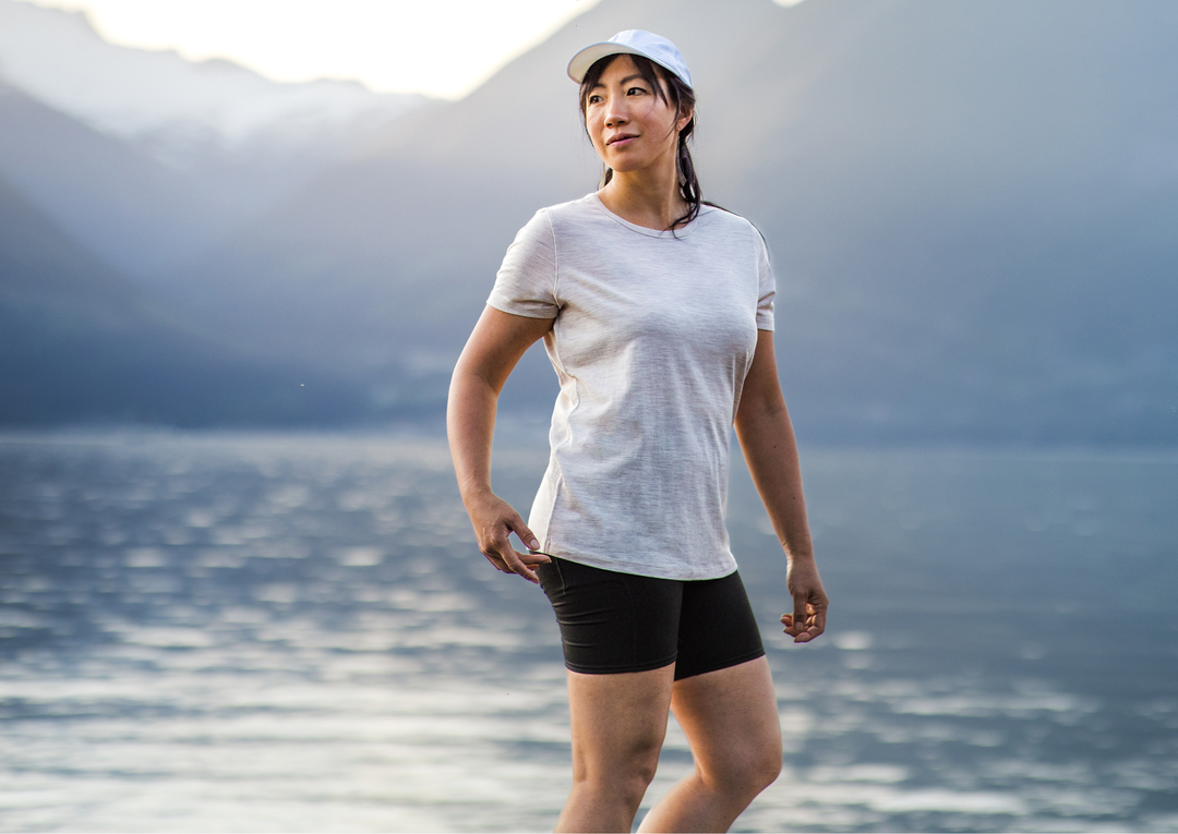 Woman in athletic wear standing by a lake with mountains in the background