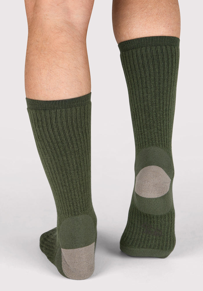 A close-up of the back of a person's lower legs wearing Woolx Mens Core Crew Socks in Winter Moss, featuring light gray heel patches. These moisture-wicking merino wool socks offer comfortable, odor-resistant protection.