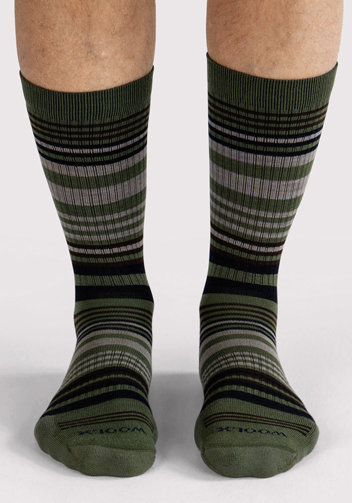 A front view of legs in Woolx Mens Everyday Crew Socks - Winter Moss Stripe, featuring green cushioning and horizontal black, gray, and olive stripes against a plain light background.
