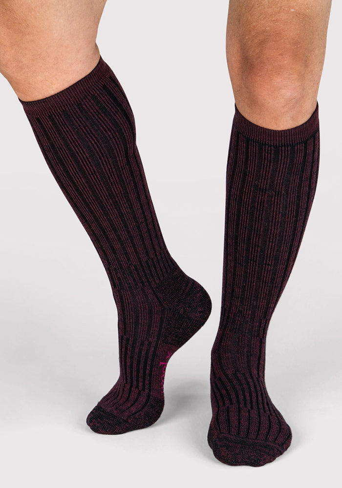 A person stands on a light gray background wearing Woolx Mens Joey Mid Calf Socks in Warm Violet.