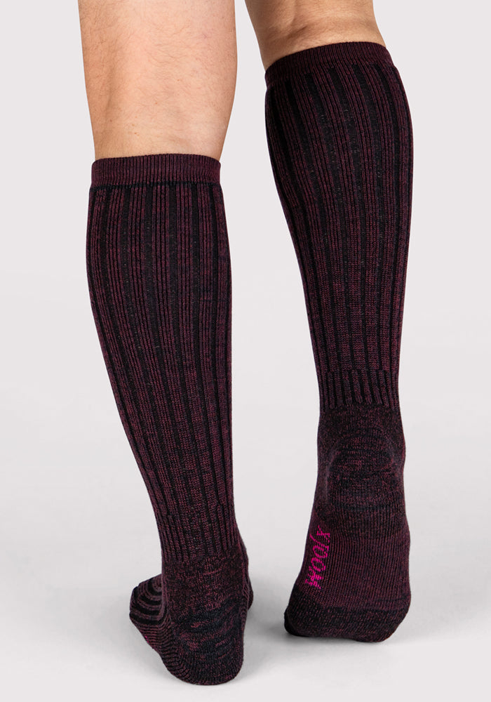 A person stands on a light surface wearing Woolx Mens Joey Mid Calf Socks in Warm Violet. The ribbed, moisture-wicking socks reach below the knee and feature dark purple and black colors. The view is from behind, showing both legs and feet.