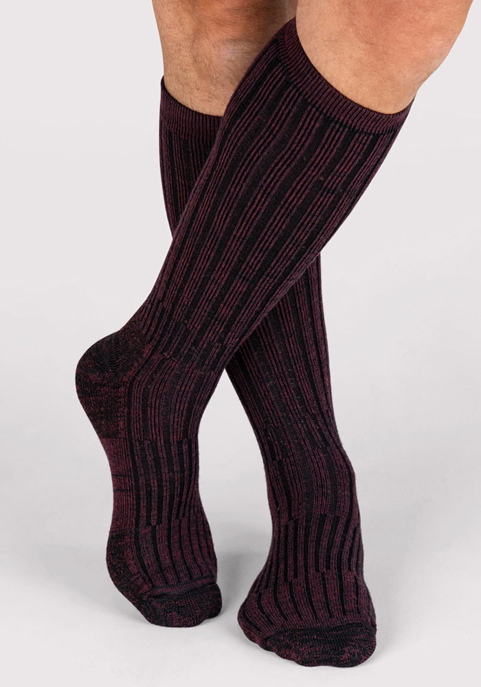 A person wearing Woolx Mens Joey Mid Calf Socks in Warm Violet stands with one leg crossed in front of the other against a plain light background.