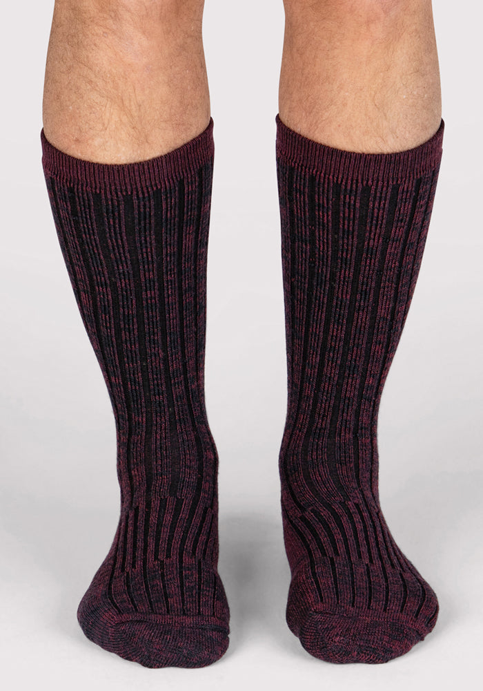 A pair of legs wearing Woolx Mens Joey Crew Socks in Warm Violet—knee-high, ribbed, with a black and burgundy pattern—stand on a white background.