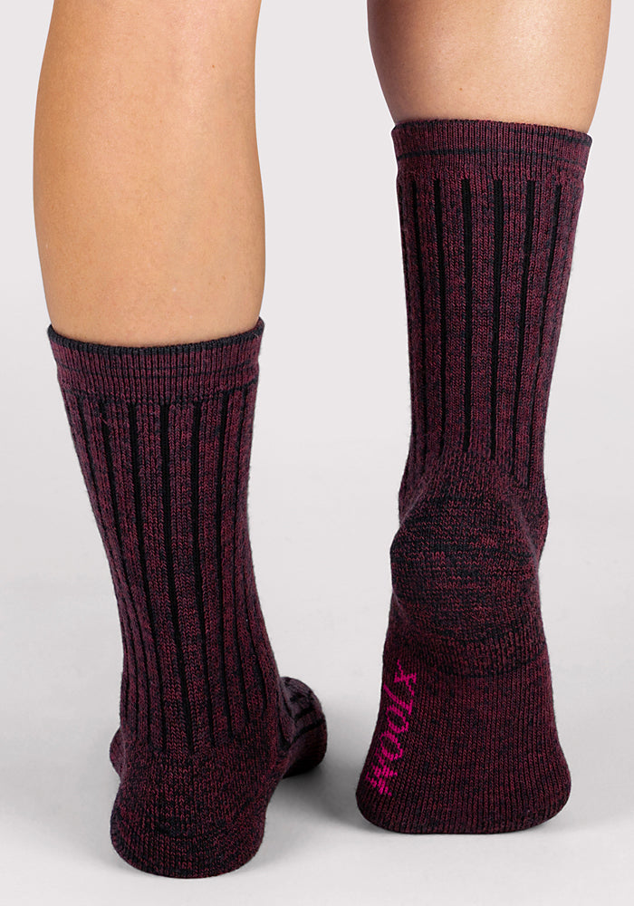 A close-up of a person’s lower legs wearing Woolx Womens Joey Crew Socks in Warm Violet, mid-calf length with black ribbed details and "XTM" in pink on one sole.