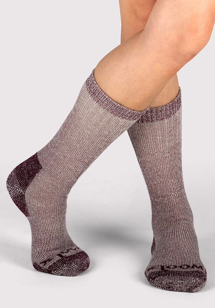 A person wearing Woolx Womens Extreme Crew Socks in Windsor Wine stands with legs crossed at the ankles against a plain light gray background.