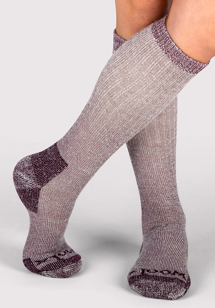 A close-up of two legs in Woolx Womens Extreme Over The Calf Socks - Windsor Wine, heavyweight with reinforced toes, heels, and cuffs in heathered gray and maroon, perfect for cold weather, set against a plain light background.