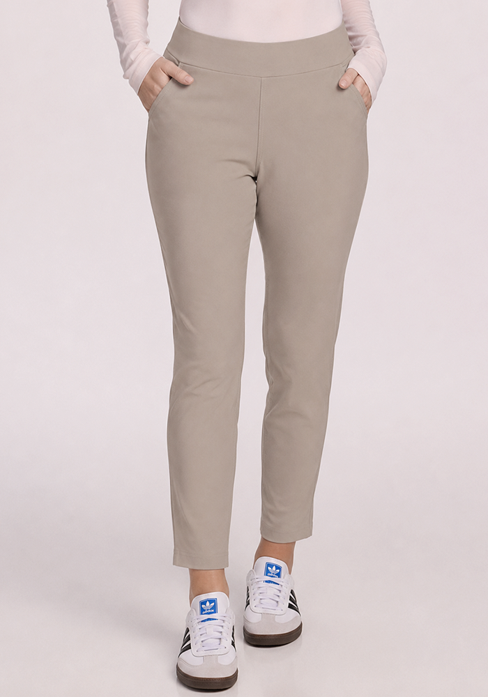 Person wearing Woolx Nicole Ankle Pants in Vintage Khaki and white sneakers with a blue logo, hands in pockets.
