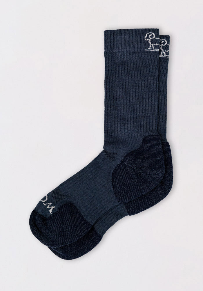 The Woolx Mens Harbor Crew Sock - Evening Tide is a dark blue, odor-resistant sock with black heels and toes, featuring a small white embroidered stick-figure design near the top. The socks are shown neatly stacked on a light background.