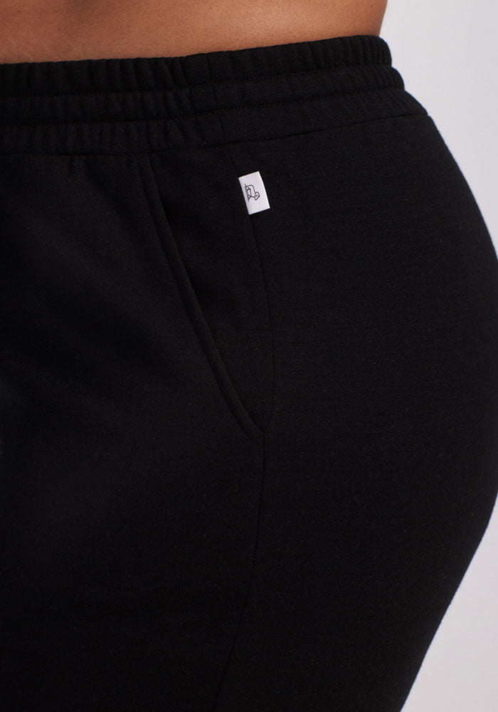 Close-up of a person wearing Woolx Parker Sweatpants in black, featuring an elastic waistband and a small white tag, highlighting the hip and upper thigh for optimal temperature regulation.