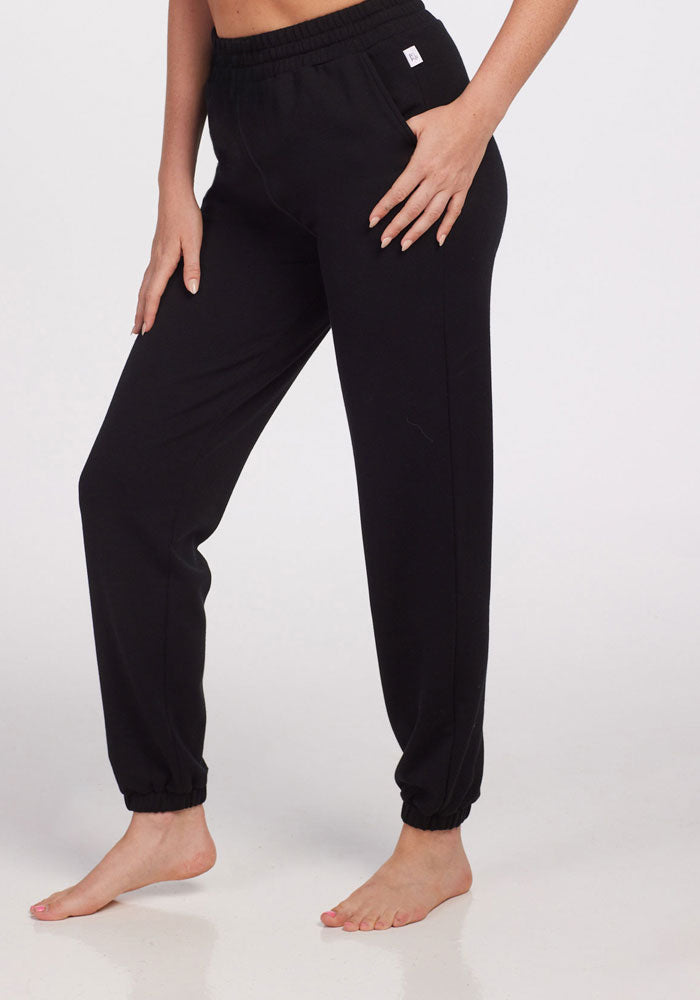 A person poses barefoot in Woolx Parker Sweatpants - Black, featuring an elastic waistband and cuffs, against a plain white background—demonstrating moisture-wicking comfort and natural temperature regulation.