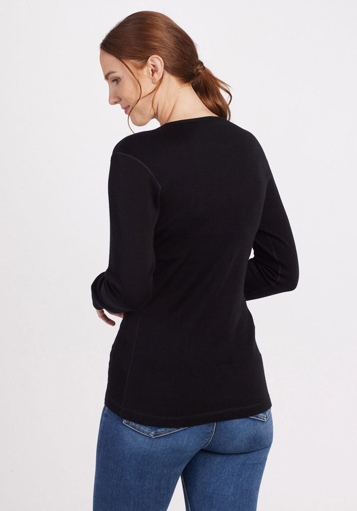 Woman with brown hair in a ponytail wears a Woolx Hannah Petite Long Sleeve Top in black and blue jeans, facing away.