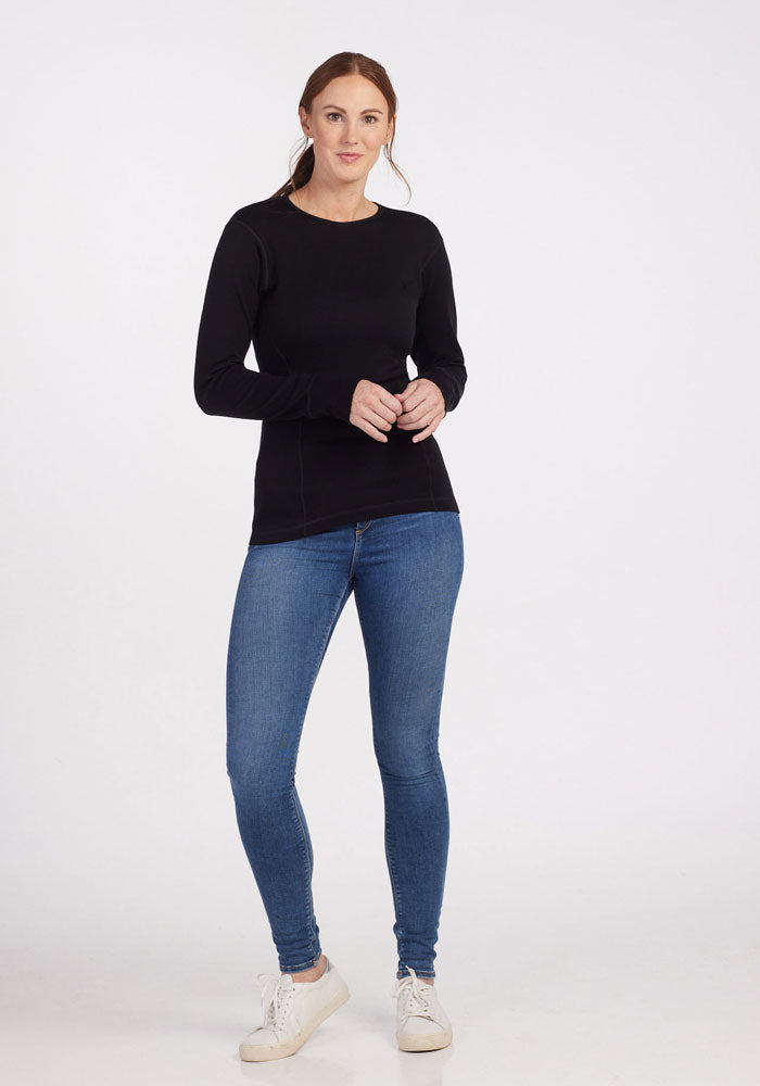 Model wears the Woolx Hannah Petite Long Sleeve Top in black, blue jeans, and white sneakers against a white background.