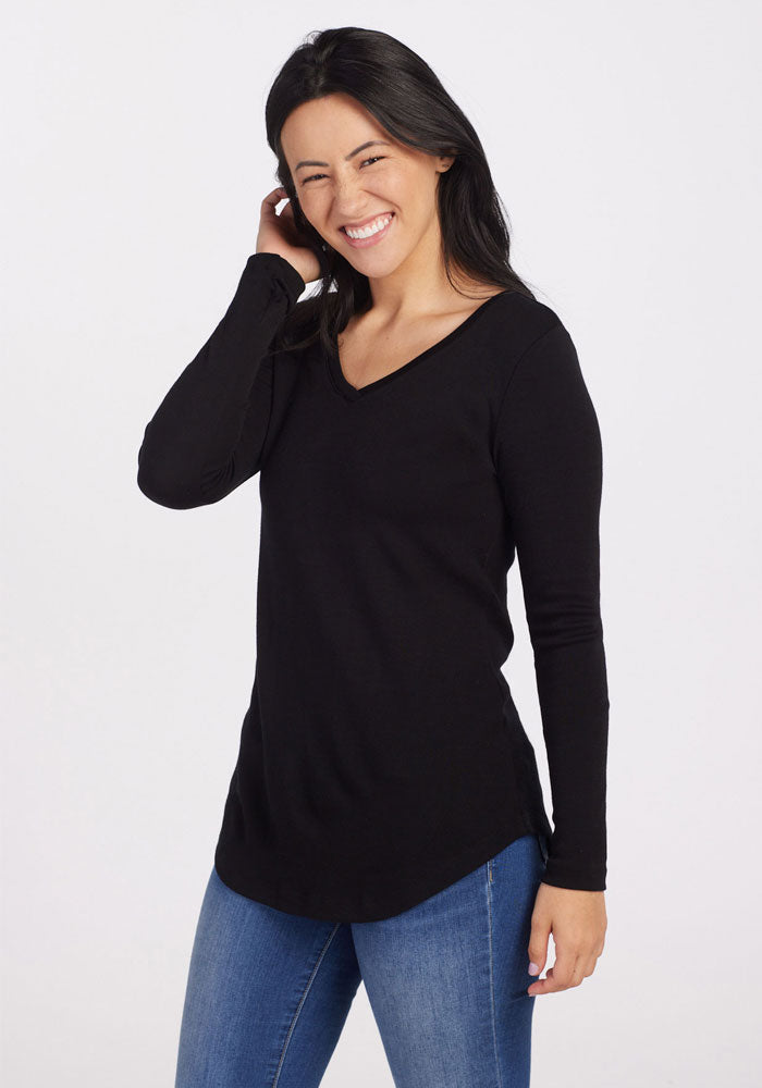 Woman smiles in Woolx Eva Petite Tunic - Black and blue jeans, standing before a plain white background.