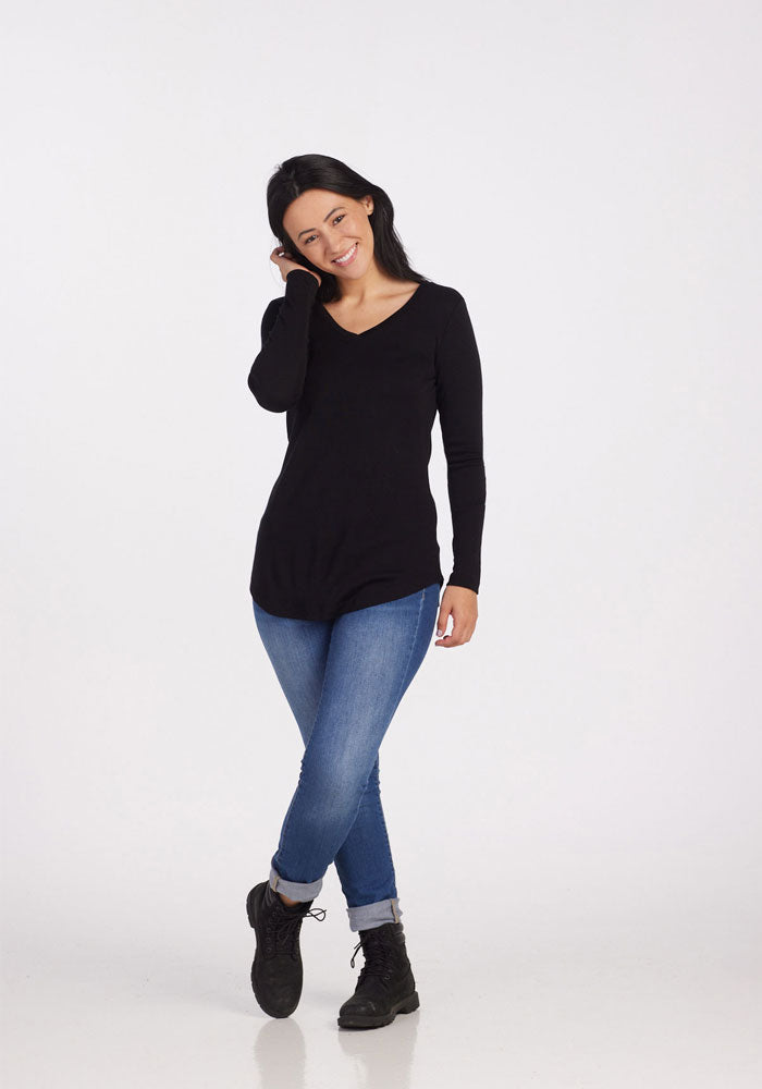 Smiling woman in Woolx Eva Petite Tunic - Black and blue jeans, hand in hair, against a white background.