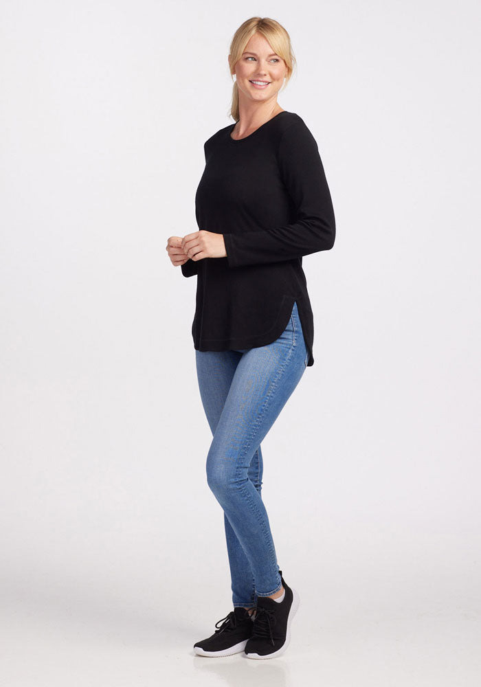 Woman wears the Woolx Blair Petite Tunic in black, blue jeans, and black sneakers, smiling against a white backdrop.