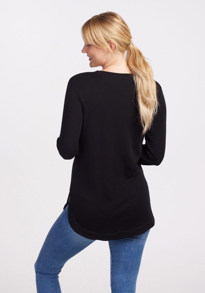 Woman with long blonde hair wears the Woolx Blair Petite Tunic in black and blue jeans, facing away from the camera.