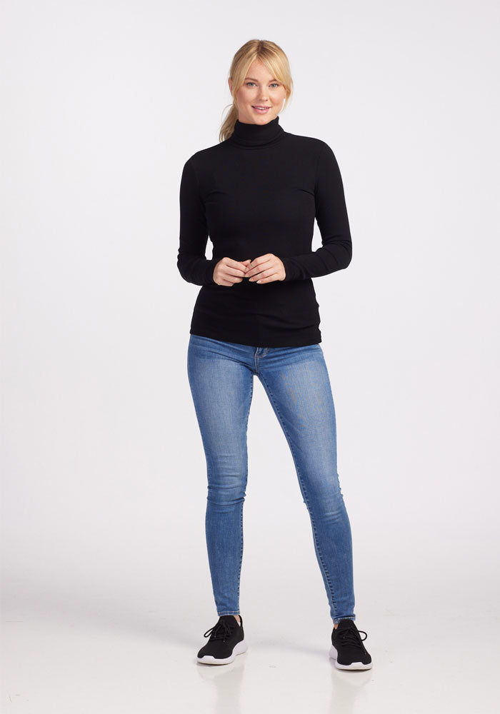 Woman in Woolx Sage Petite Ribbed Turtleneck - Black, blue jeans, and black sneakers against a white background.
