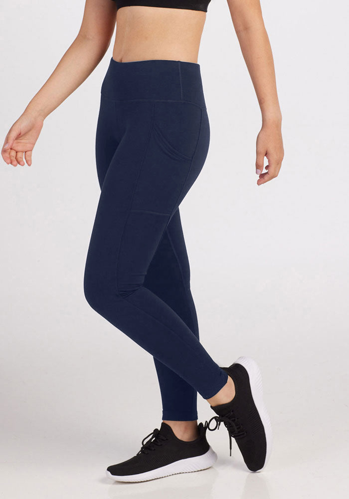 A person wears a black crop top, Woolx Piper Pocket Leggings in Deep Navy, and black athletic shoes with white soles, standing against a plain light background.