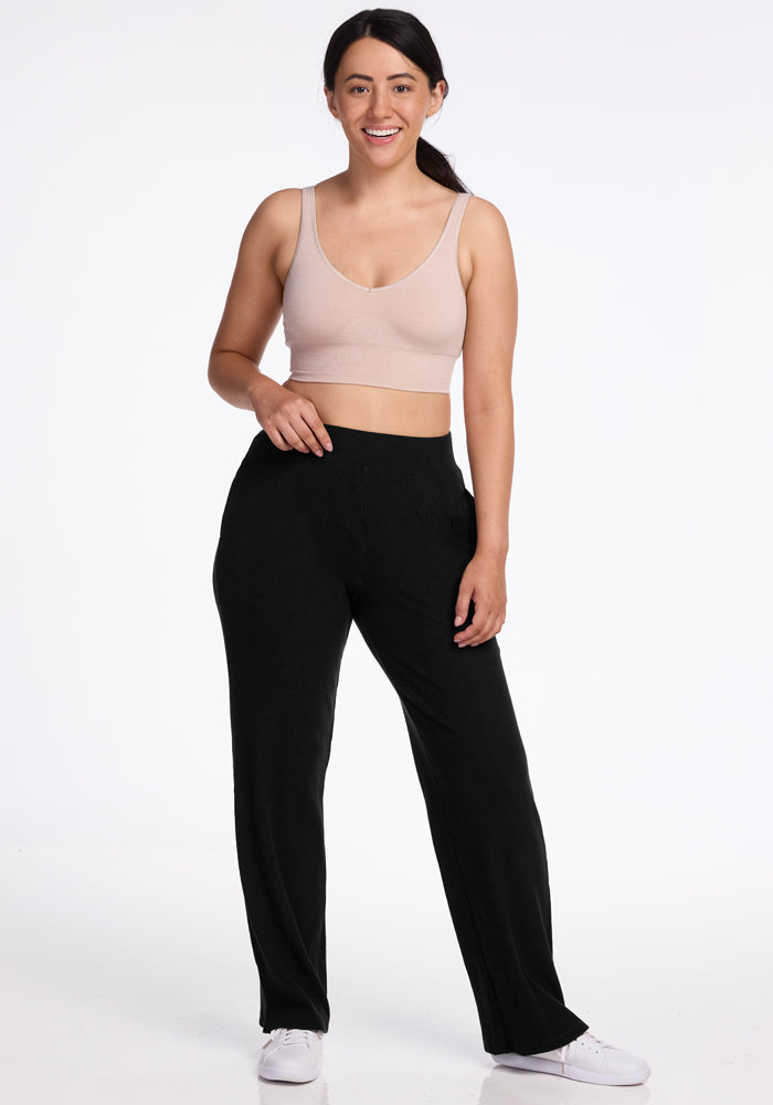 Woman in Luca Petite Pants - Black by Woolx, beige crop top, and white sneakers smiles against a white background.