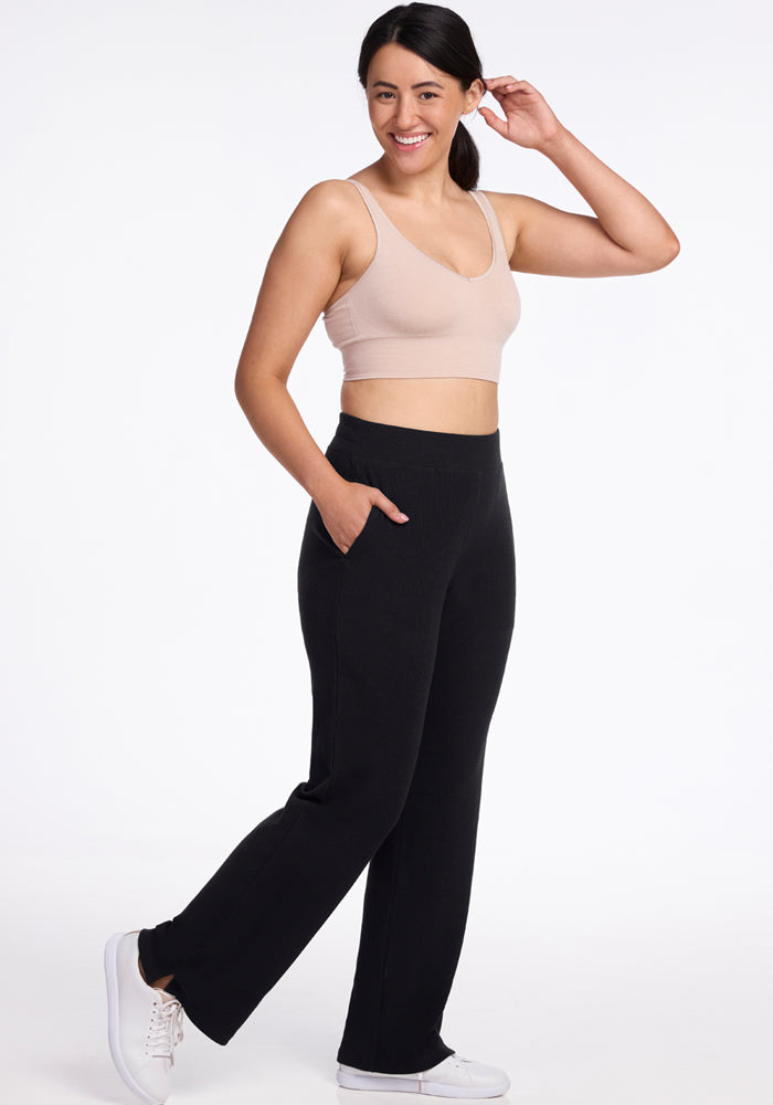 Woman in Woolx Luca Petite Pants - Black, beige sports bra, and white sneakers smiles with hand near her ear.